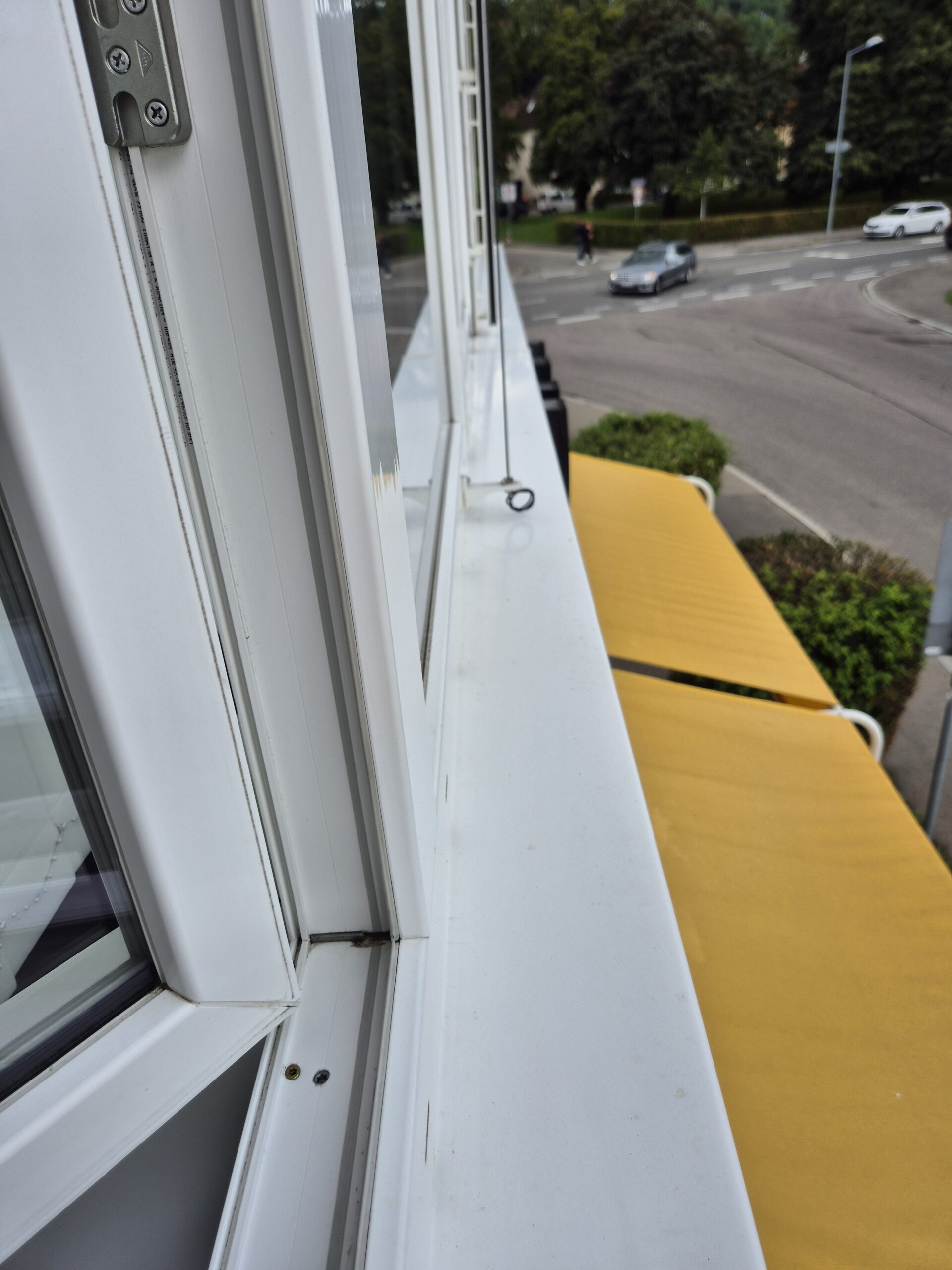 Offenes Fenster über den Straßenbahnen, gelbe Markise und Gebäudereinigungsdienst unten.