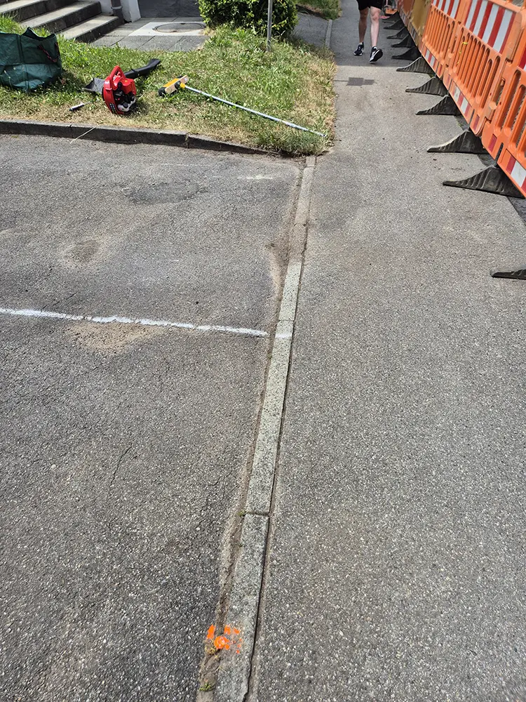 Ein Gehweg mit Werkzeugen der Grauflächenpflege, Absperrungen und einer Person, die weggeht.